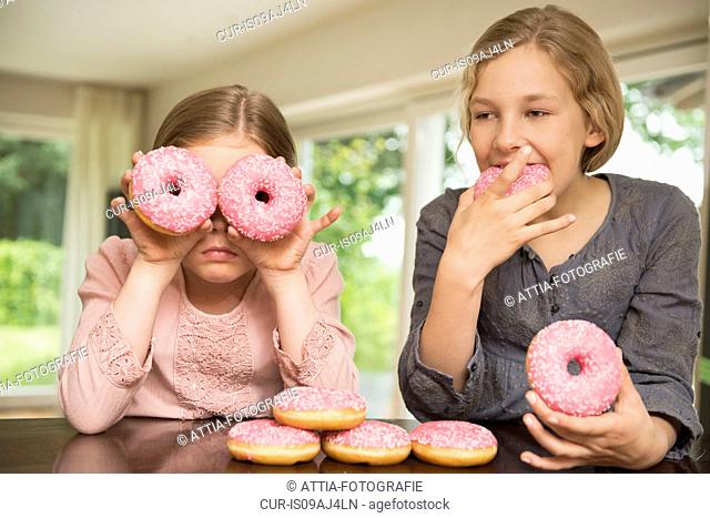 Two sisters one with doughnut holes over her eyes, the other eating