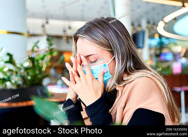 Gestresste und erschöpfte Frau mit Mundschutz bei Covid-19 Pandemie in einem Cafe
