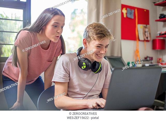 Teenage girl watching boy using laptop