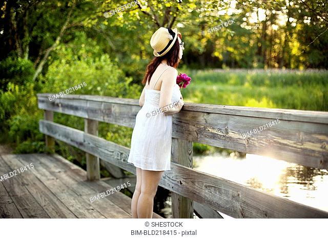 Caucasian woman standing on bridge over rural pond