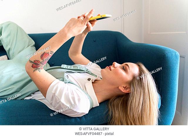 Young woman lying on couch using cell phone