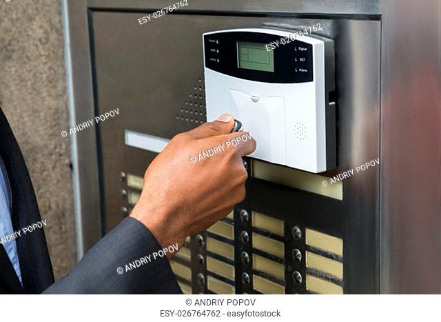 Close-up Of Businessperson's Hand Using Remote Control For Operating Door Security System