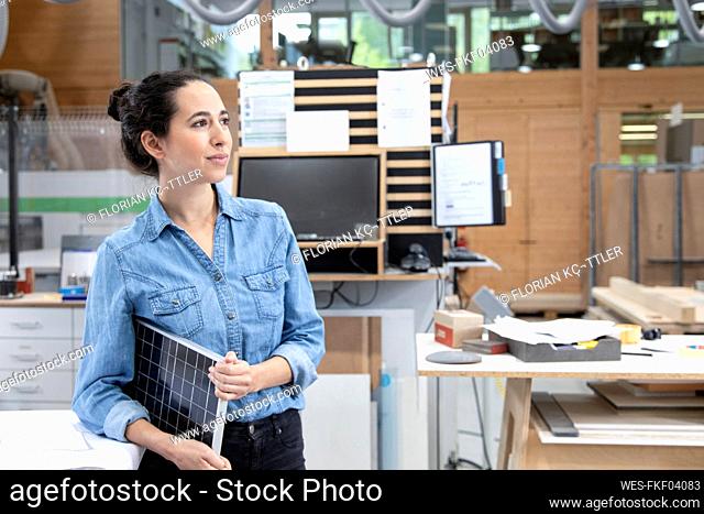 Thoughtful businesswoman holding solar panel model concept while looking away in factory