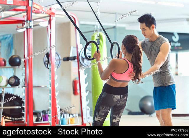 Low-angle view of a beautiful young woman smiling while doing push-ups on gymnastic rings during workout at the gym