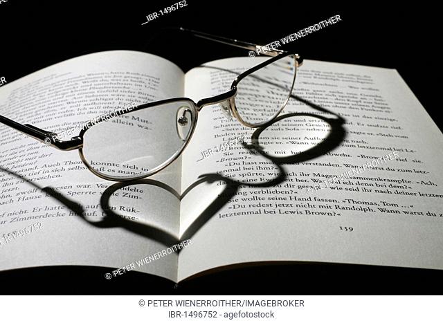 Book, pair of reading glasses, heart-shaped shadow