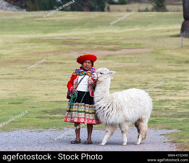 Peruvian woman in her traditional dress holding an alpaca by her side at the ruins of Saqsaywaman