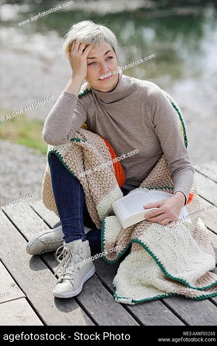 Mature woman with book and blanket sitting on pier