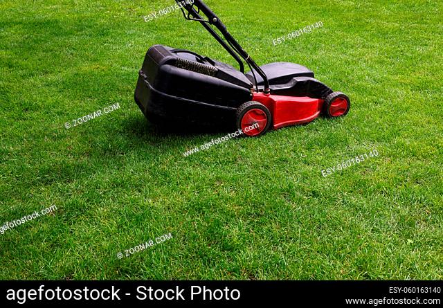 Electric mower over background of green grass lawn sunny summer day, high angle view, side view