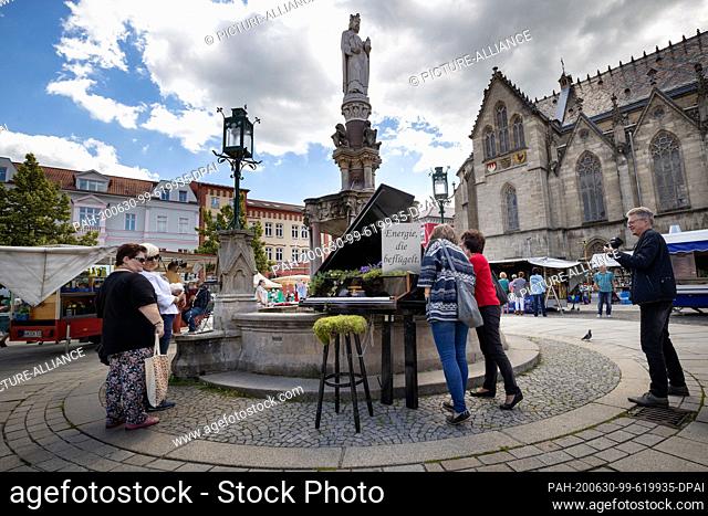 30 June 2020, Thuringia, Meiningen: People look at the piano in the Heinrichsbrunnen in front of the town church. Overnight