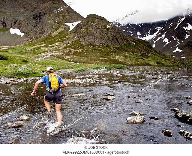 Trail runner splashes through Middle Fork Campbell Creek while running Mount Elliot to Wolverine Peak to Rusty Point, Chugach Moutains, Chugach State Park