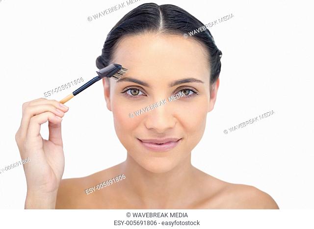 Peaceful young brunette using eyebrow brush