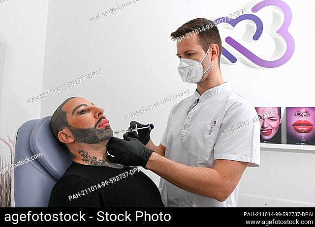 13 October 2021, Berlin: Fashion designer Harald Glööckler (l) has his cheeks injected by Milos Zoric at the Medicalthree plastic surgery clinic on...