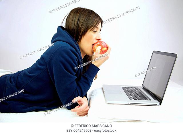 Woman eating red apple in front of computer laying in bed