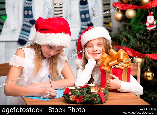 Christmas holiday indoor craft. Little girl sitting at the table and waiting for New Year celebration. One girl writing Christmas celebration to parents