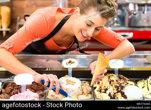 Young saleswoman in an ice cream parlor takes a scoop of ice cream