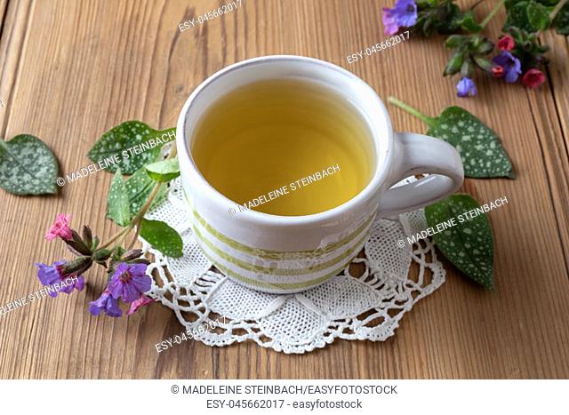 A cup of herbal tea with fresh lungwort, or pulmonaria flowers on a table