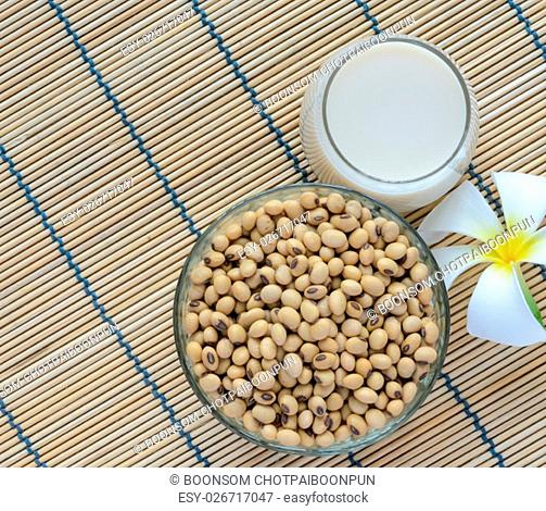 Fresh Soy milk (Soya milk) and dried soybean seeds on bamboo place mat with white plumeria flower. Traditional staple of East Asian cuisine