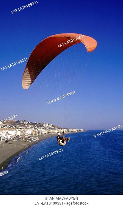 Rincon de la Victoria. Cliffs on coast. Person paragliding with wide red sail. View of beach, town. Sea