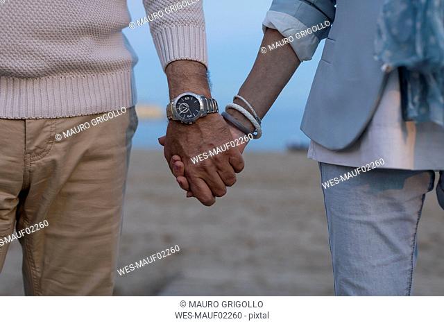 Close-up of senior couple hand in hand on the beach at dusk