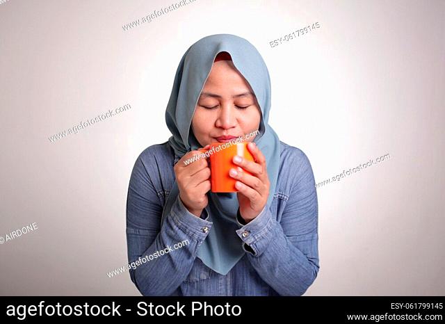 Portrait of happy young beautiful Asian muslim woman smiling, drinking tea or coffe during coffee break