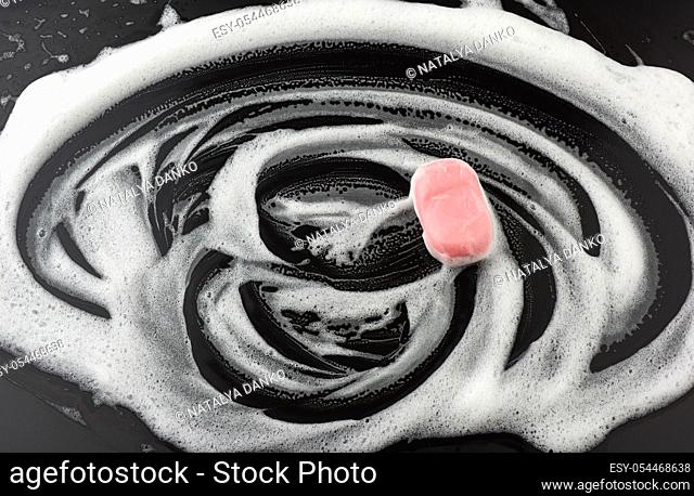 white soap foam and pink soap on a black background, top view, concept of cleanliness, antibacterial