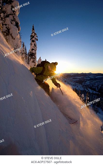 A female skier descends a slope at sunset in the Whitewater Winter Resort backcountry, British Columbia
