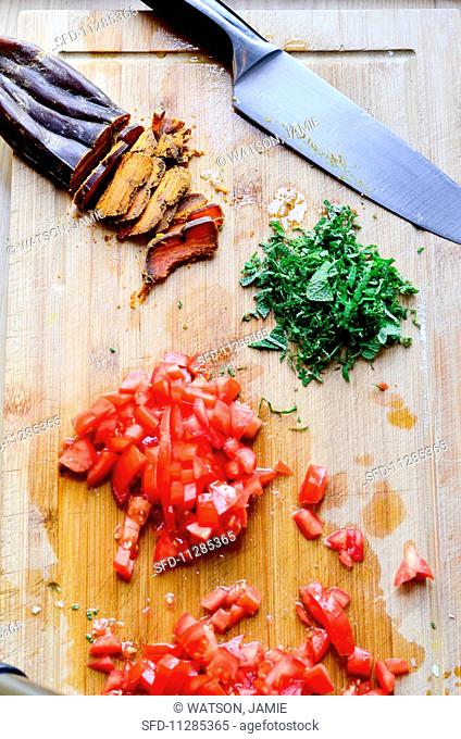 Bottarga, chopped tomatoes and basil with a knife in chopping board