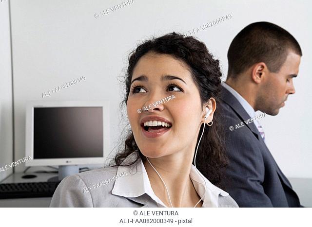Woman listening to earphones and daydreaming in office