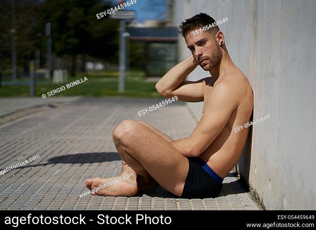 Portrait of a pretty guy dressed in underwear on a concrete wall