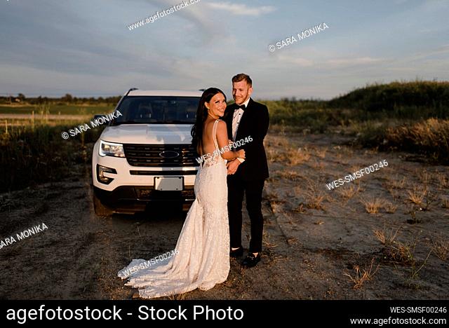 Smiling woman with male partner standing against car in field