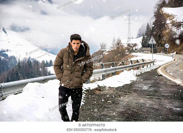 Young man walking on roadside under the snow up in the mountains. Snowy mountain on background