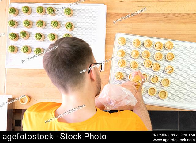 06 April 2023, Saxony, Dresden: Sebastian Pietsch, master baker, fills round dough molds made from field bean flour with a paprike feta paste at the ""Qioback""...