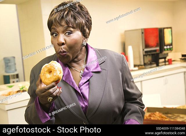 Black businesswoman eating donuts in office