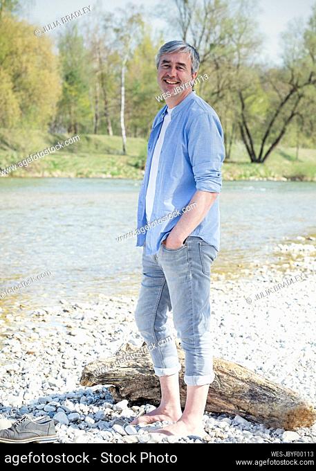 Happy man with hand in pocket standing by river