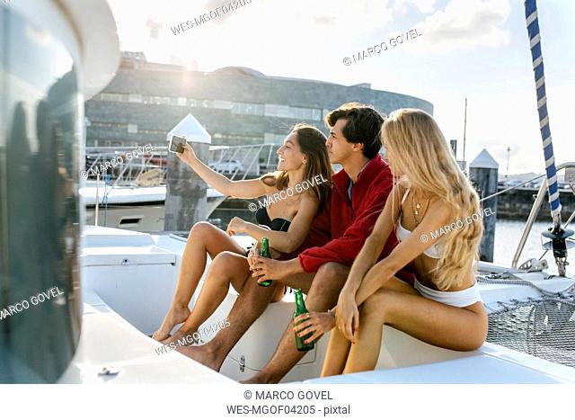 Three young friends enjoying a summer day on a sailboat, taking a selfie
