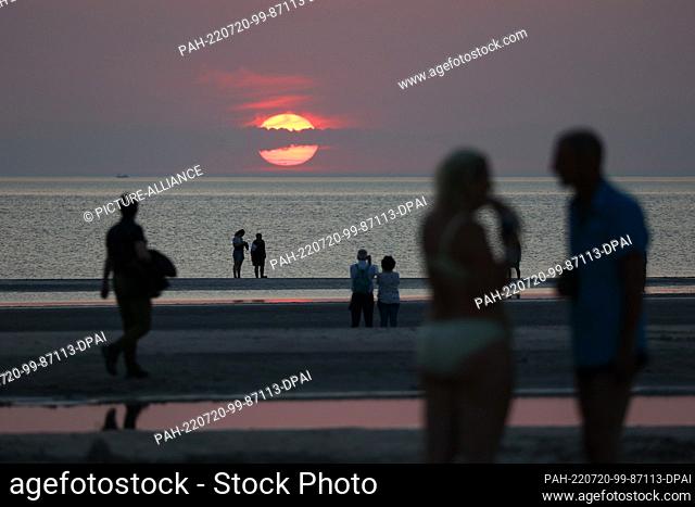19 July 2022, Schleswig-Holstein, St. Peter Ording: Visitors are on the beach in St. Peter-Ording in the evening at sunset and summer temperatures