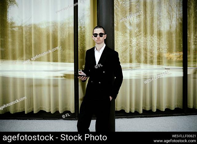 Businessman holding mobile phone in front of window