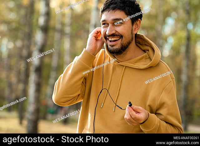 Happy man listening to music through in-ear headphones in park