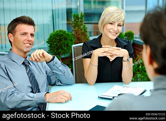 Happy business people sitting around table outdoor on office terrace and talking, smiling. Over the shoulder view