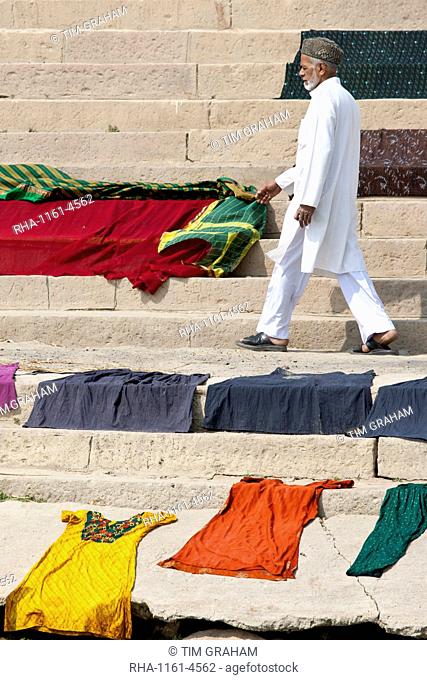 Indian man walks past laundry drying on the steps of Kali Ghat by the The Ganges River in City of Varanasi, Benares, India