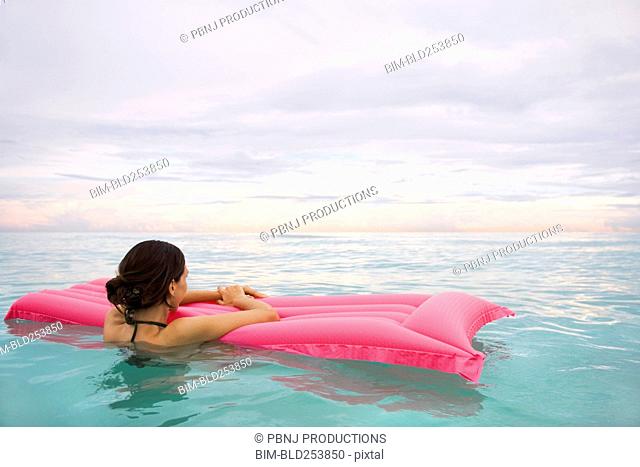 Mixed Race woman floating in ocean on inflatable raft