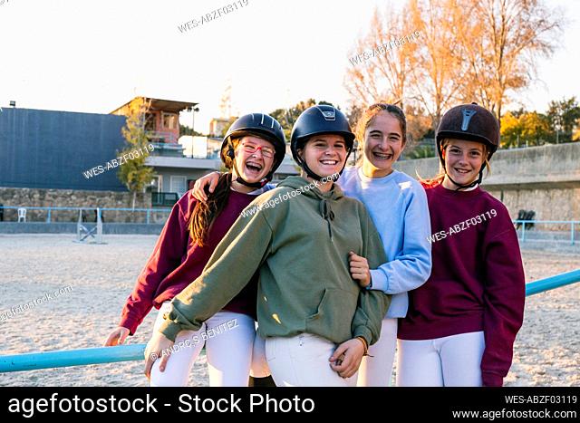 Portrait of cheerful female jockeys standing together at training ground against sky