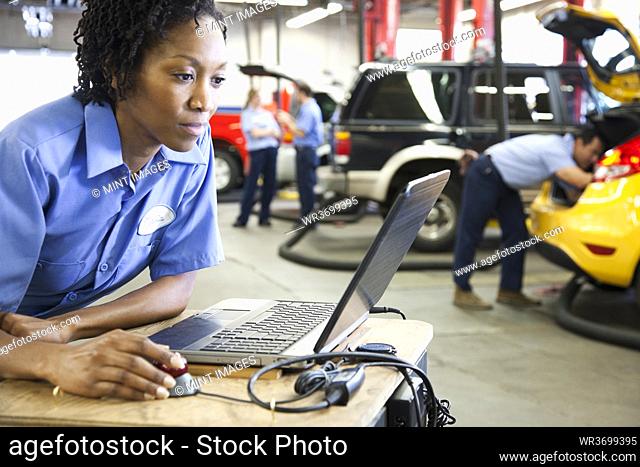 Female mechanic using a laptop, diagnostic electronics, in an auto repair shop