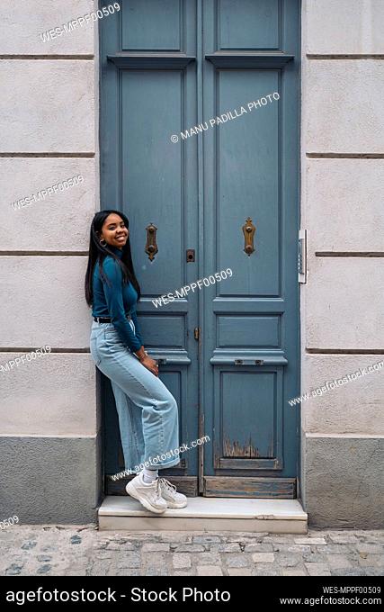 Portrait of smiling young woman standing at a door in the city