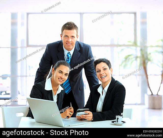 Young businesspeople talking in office lobby, looking at camera, smiling