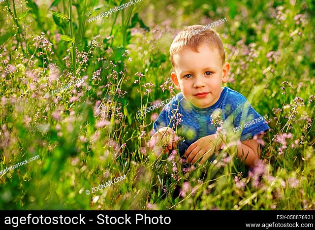 Beautiful blue-eyed little boy hiding in tall grass squatting