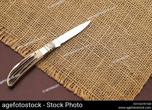 Close up photo of small folding knife on hemp cloth background