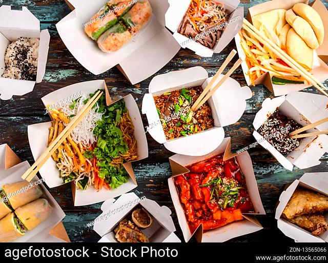 Assorted Chinese dishes in paper delivery boxes: sweet and sour chicken, dim sum, spring rolls, noodles, salad, rice, steamed buns, dips