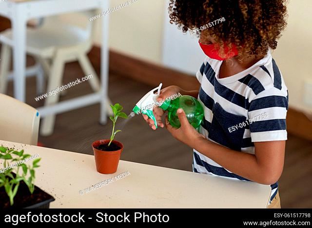 Boy wearing face mask spraying water in plant pot