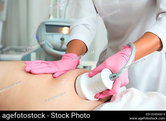 Closeup photo of fat man with big belly having cavitation procedure removing cellulite on abdomen in modern beauty clinic